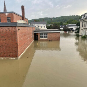 An industrial brick building surrounded by brown flood water.